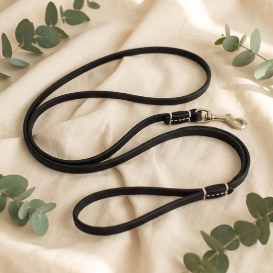 Furmonogram full-grain leather dog leash — Black, coiled on cream linen with eucalyptus