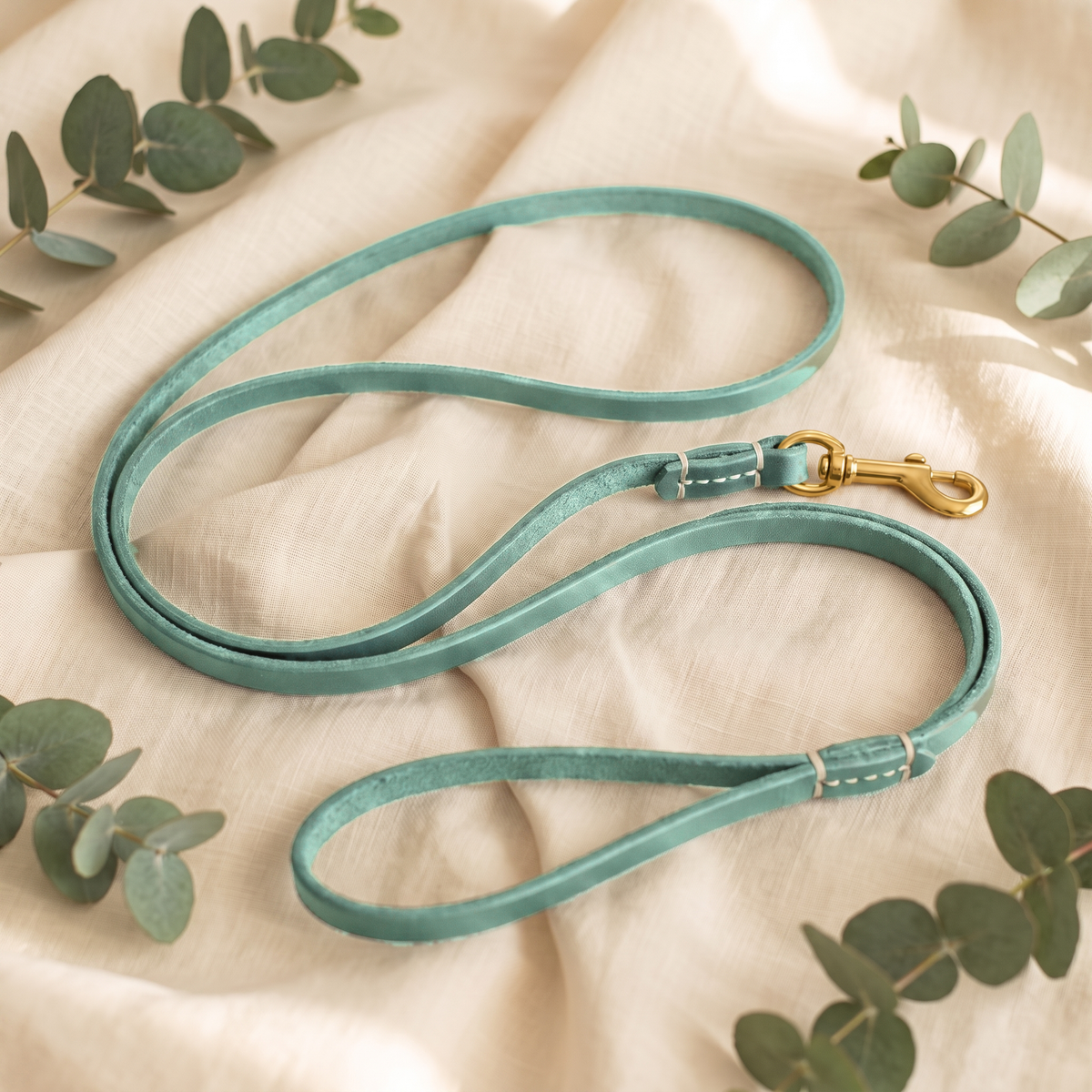 Green Furmonogram leather dog leash, coiled on cream linen with eucalyptus