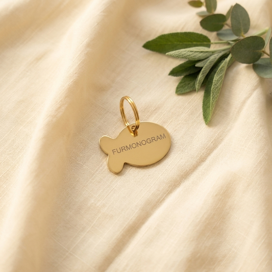 Gold Furmonogram stainless steel pet ID tag, flat lay on cream linen with eucalyptus accent